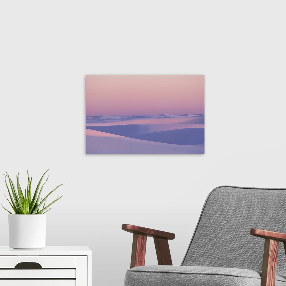 A modern room featuring Pink and purple illuminated sand dunes during sunset.