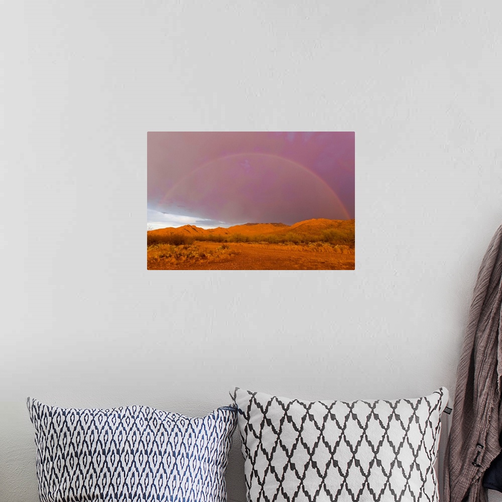 A bohemian room featuring Rainbow and purple sky on the backside of thunderstorm in a desert.