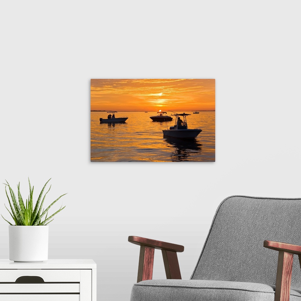 A modern room featuring Silhouetted boats and shimmering water during a picture perfect sunset.