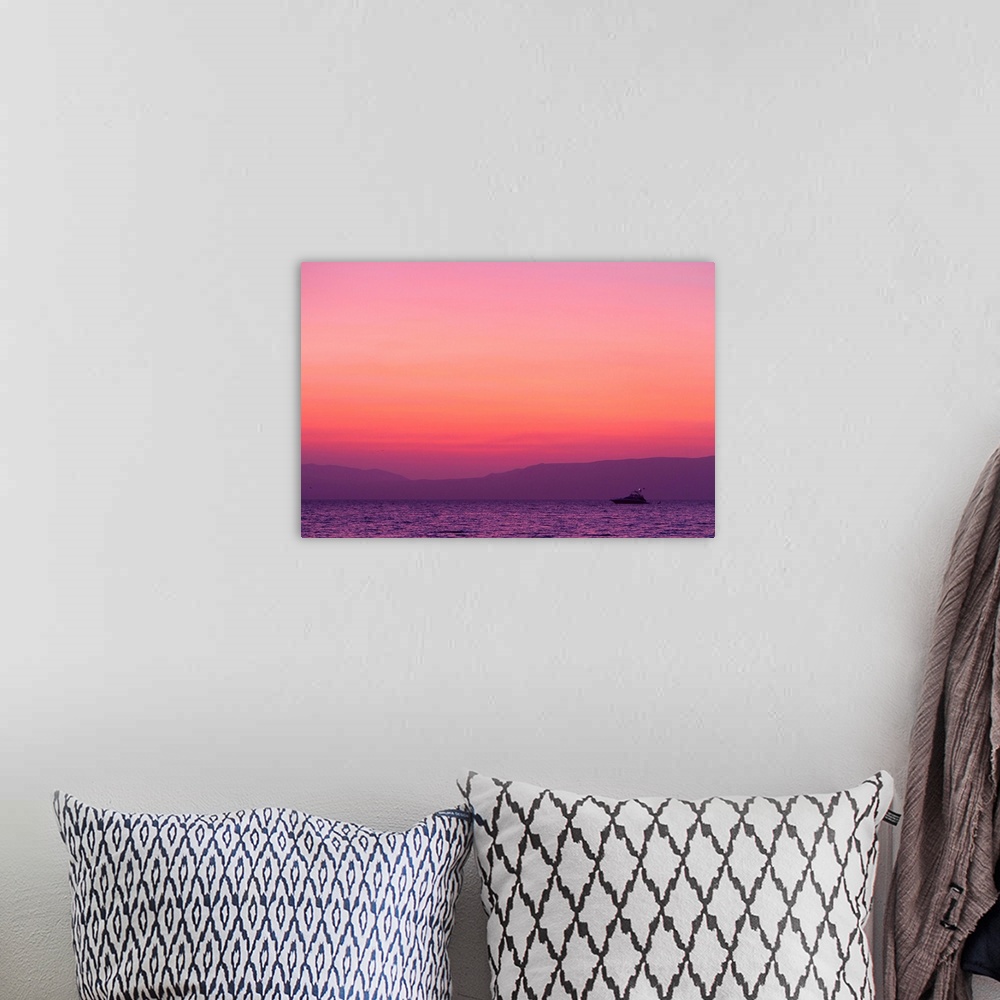 A bohemian room featuring Sunset turns the sky pink and purple as a lone boat floats offshore.