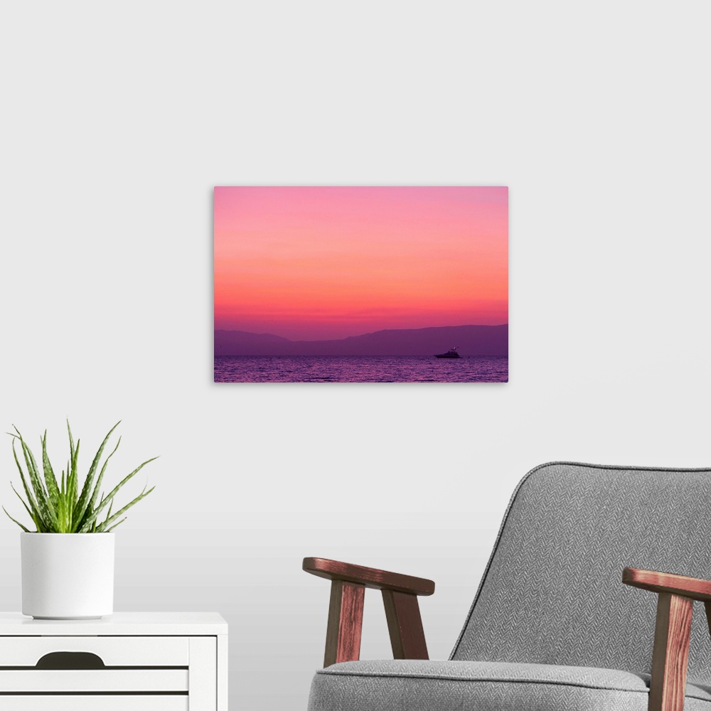 A modern room featuring Sunset turns the sky pink and purple as a lone boat floats offshore.
