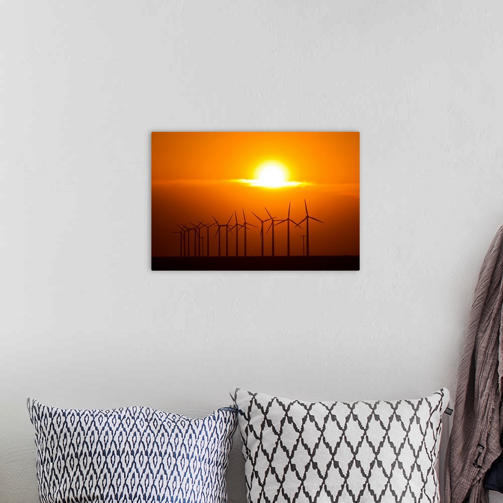 A bohemian room featuring The sun sets behind a row of spinning windmills or wind turbines.
