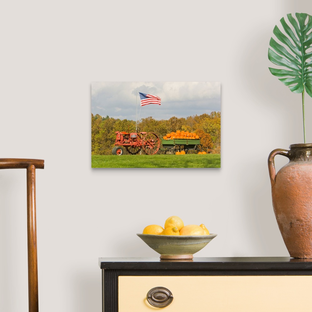 A traditional room featuring The United States flag flying over tractor wagon filled with pumpkins.