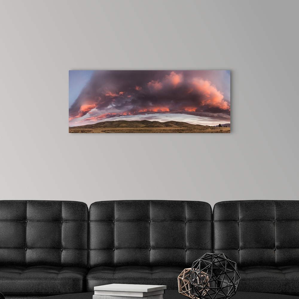A modern room featuring Dawn cloudscape arches over tussock grass covered hills, St Bathans, Central Otago, New Zealand.