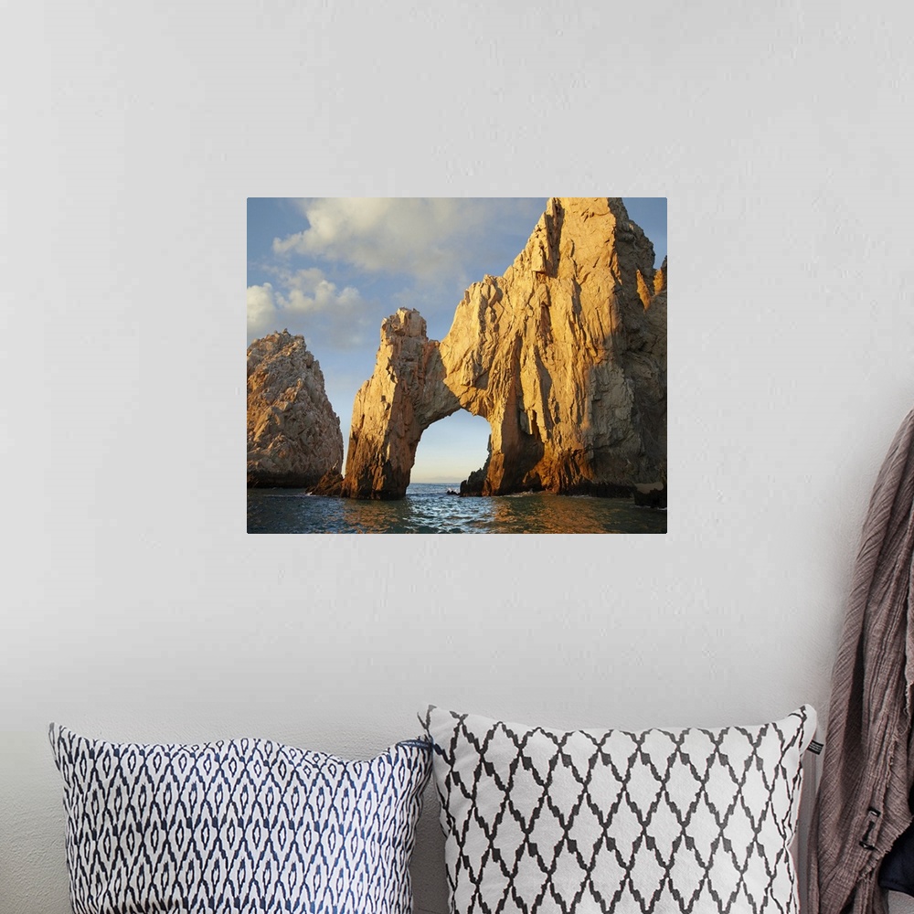 A bohemian room featuring Photograph of huge rock formation with an arch in the ocean under a cloudy sky.
