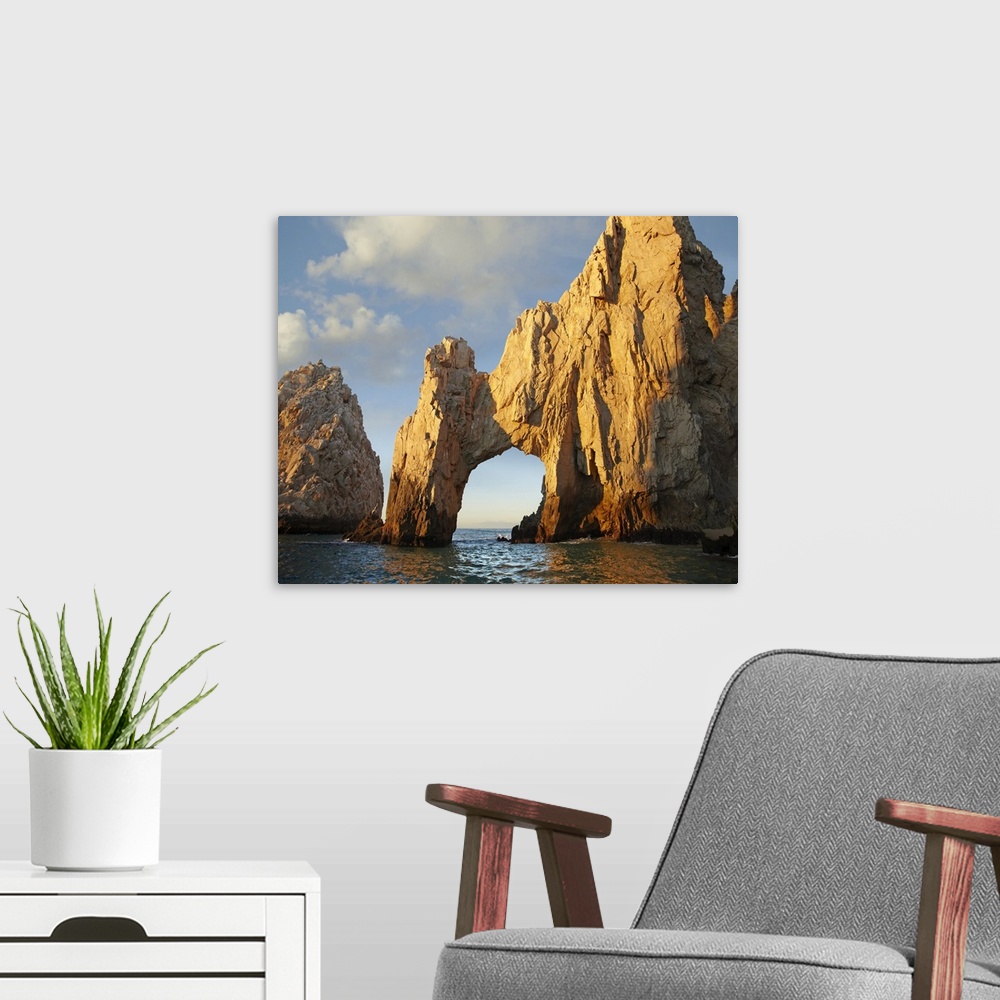 A modern room featuring Photograph of huge rock formation with an arch in the ocean under a cloudy sky.