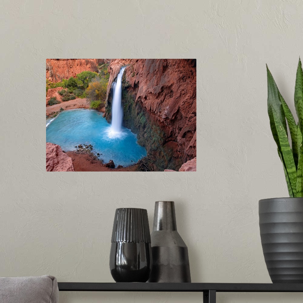 A modern room featuring Large photograph taken of a waterfall crashing into the clear water below.  This portion of the c...