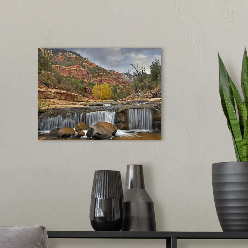 A modern room featuring Wall art of a small waterfall in a river with red rock formations in the background.