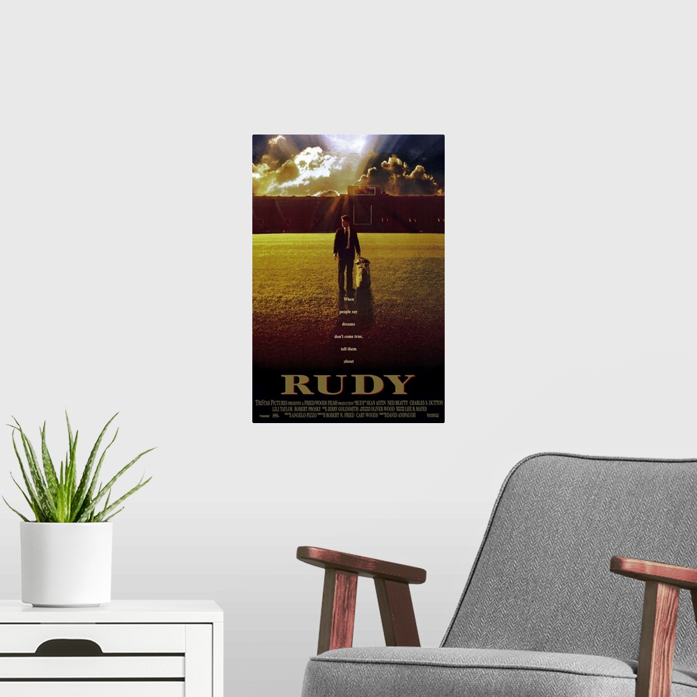 A modern room featuring This large vertical piece is a movie poster for "Rudy". It pictures the star character walking ac...