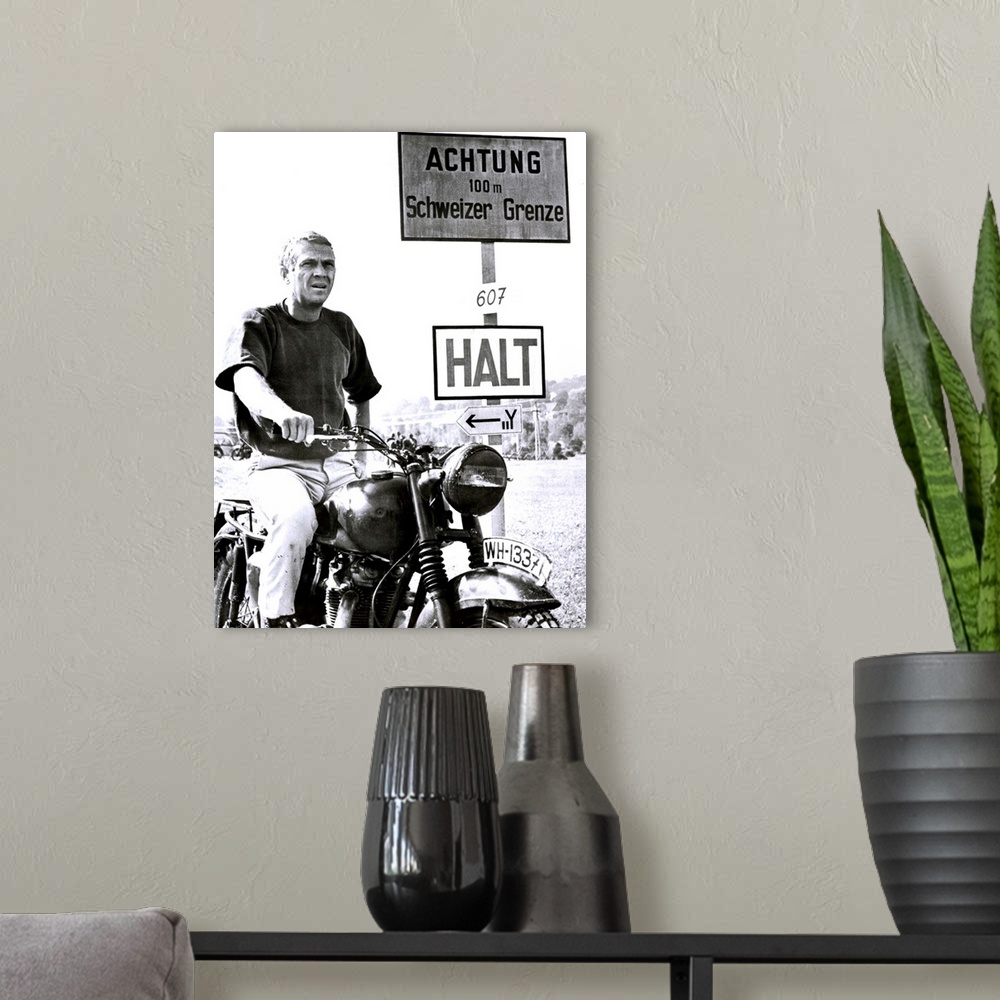 A modern room featuring Vertical movie advertisement for the 1963 film, The Great Escape.  A man sits on a vintage motorc...