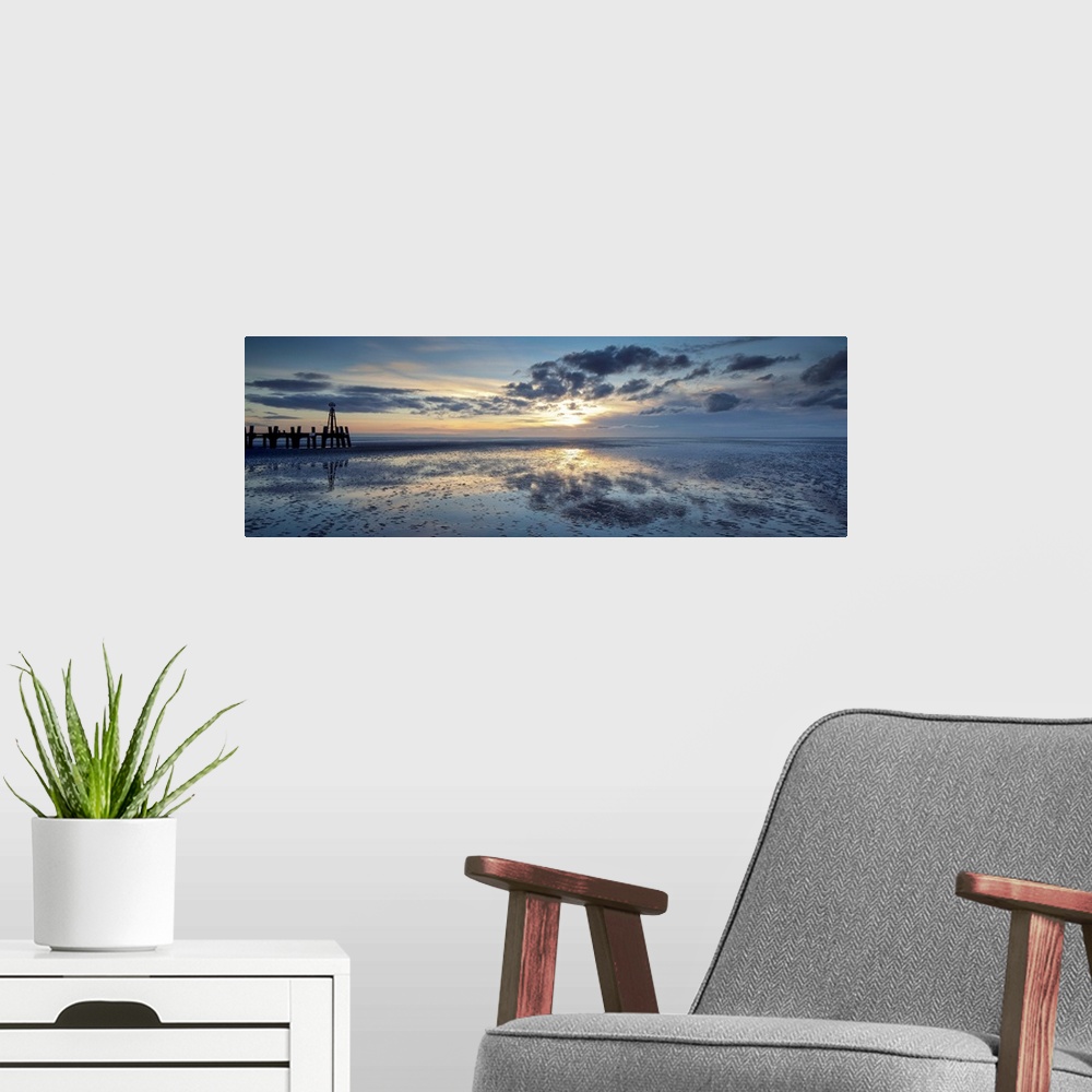 A modern room featuring A panoramic image of a tranquil golden blue dawn with fluffy clouds over reflecting wet sand with...