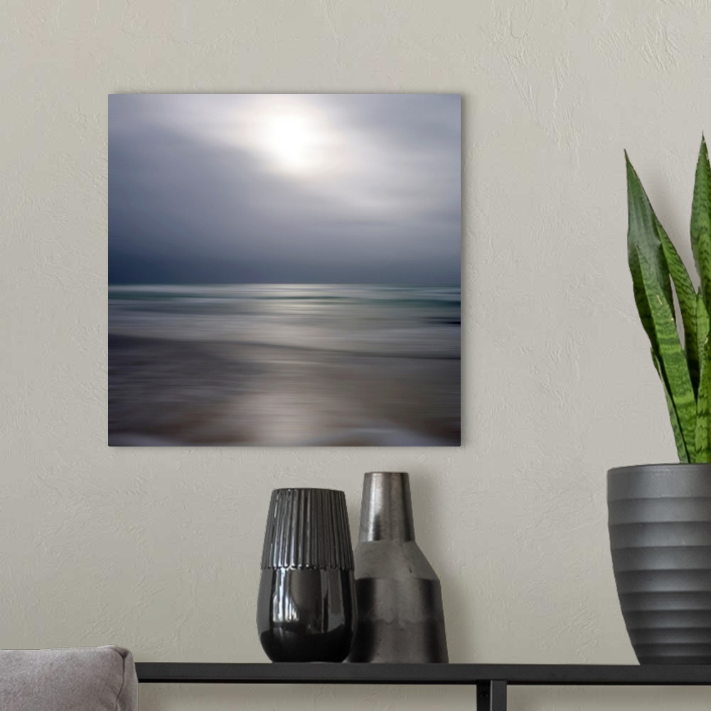A modern room featuring Giant photograph displays an ocean gently making its way to a sandy shore while underneath a clou...