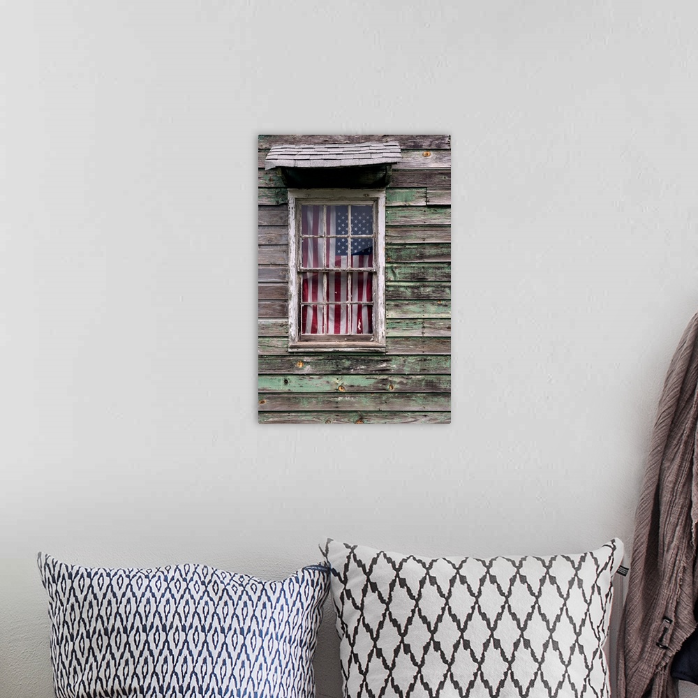 A bohemian room featuring An American Flag hanging in the window of a house with weathered wooden siding.