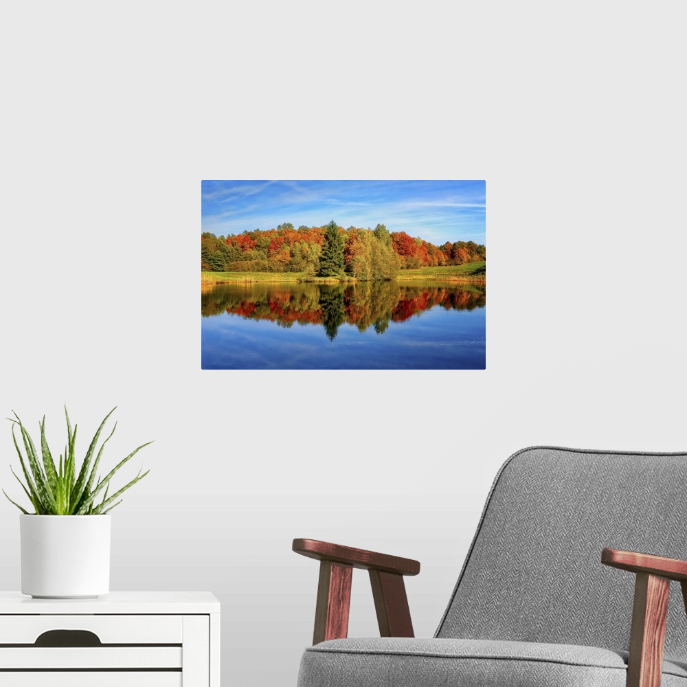 A modern room featuring Trees in a variety of fall colors mirrored in a lake with a blue sky above.