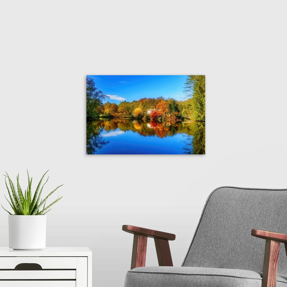 A modern room featuring Colorful trees in the fall and a deep blue sky reflected in the calm waters of a lake.