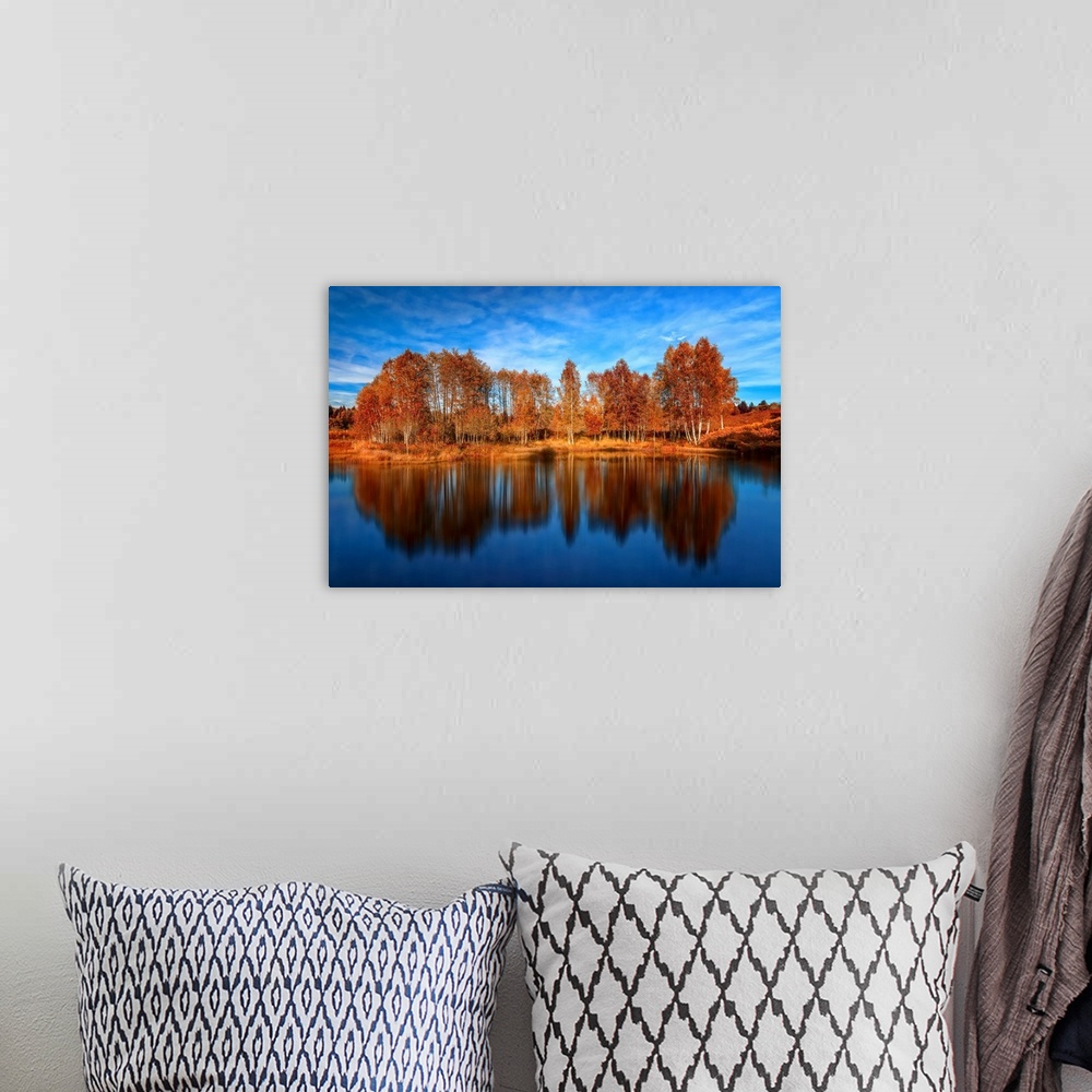 A bohemian room featuring Bright orange trees reflected in the deep blue water of a lake.