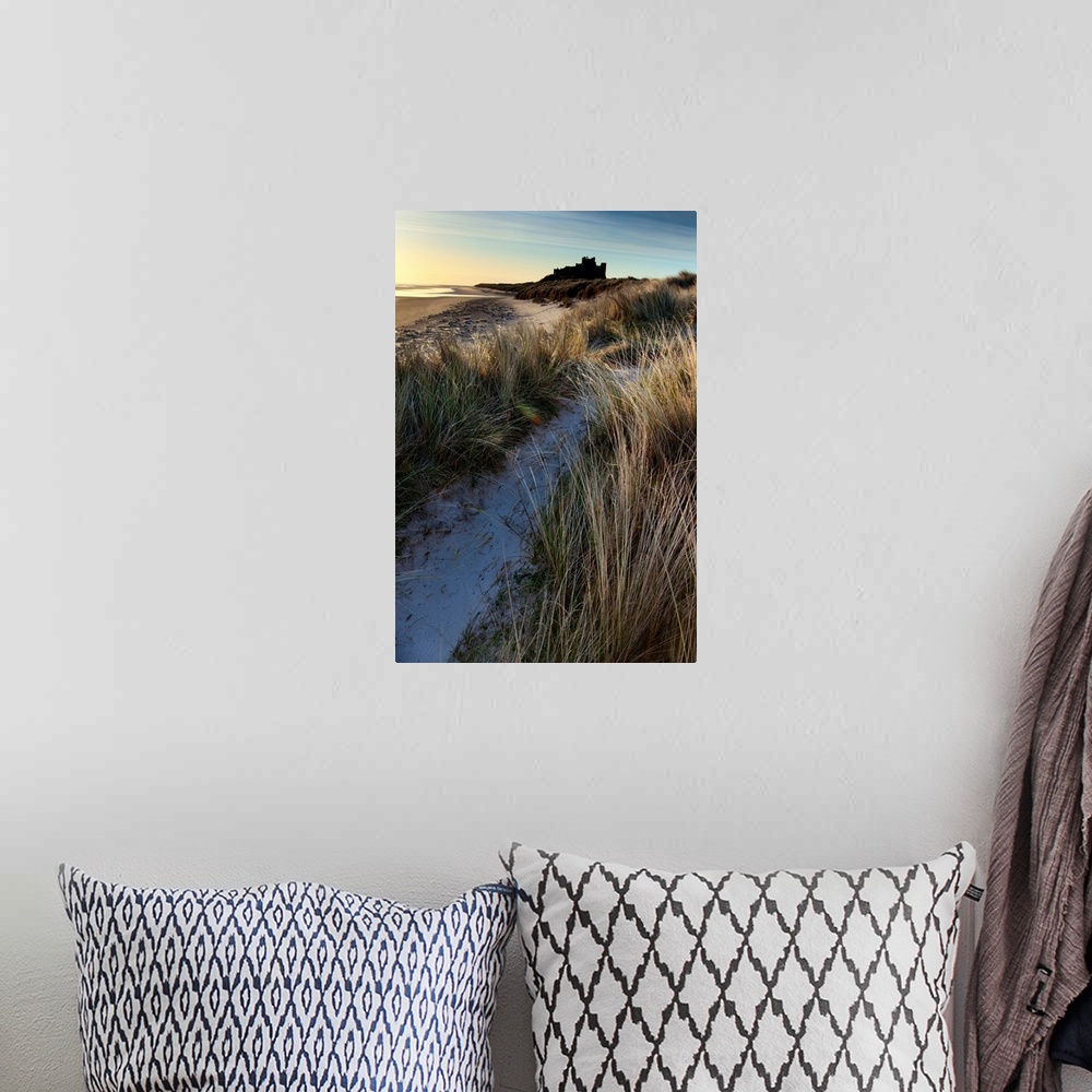 A bohemian room featuring Bamburgh Castle, Northumberland, UK lit by soft golden light with a blue sky over windsept marram...