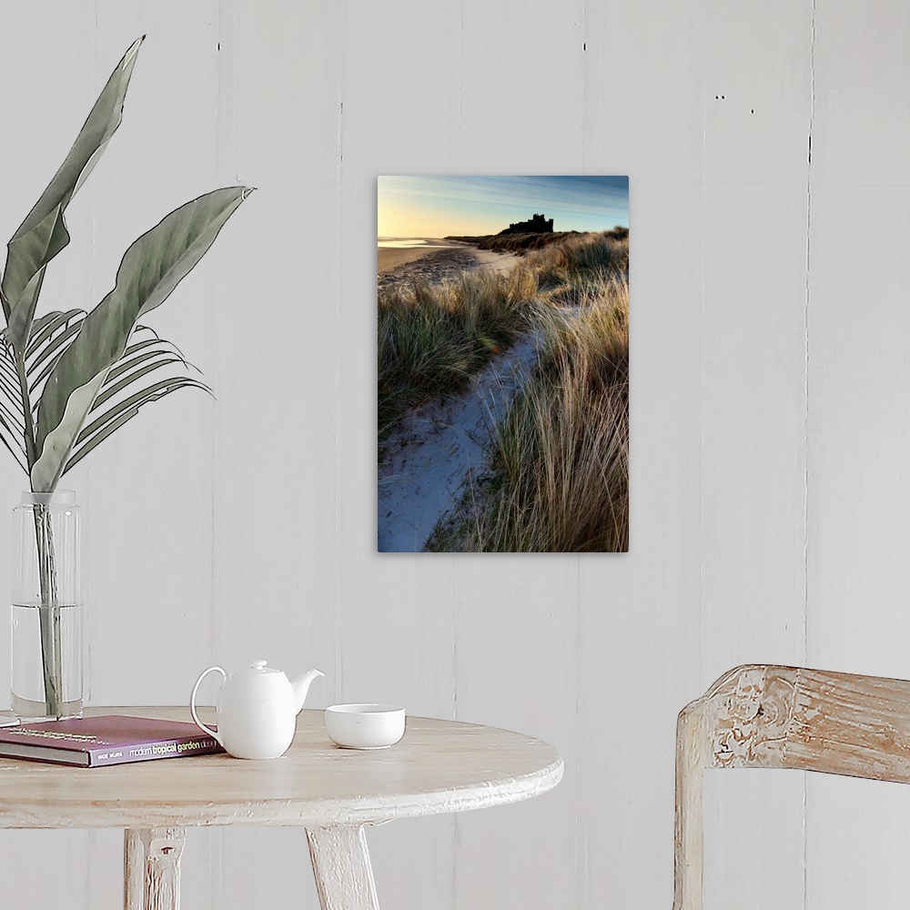 A farmhouse room featuring Bamburgh Castle, Northumberland, UK lit by soft golden light with a blue sky over windsept marram...