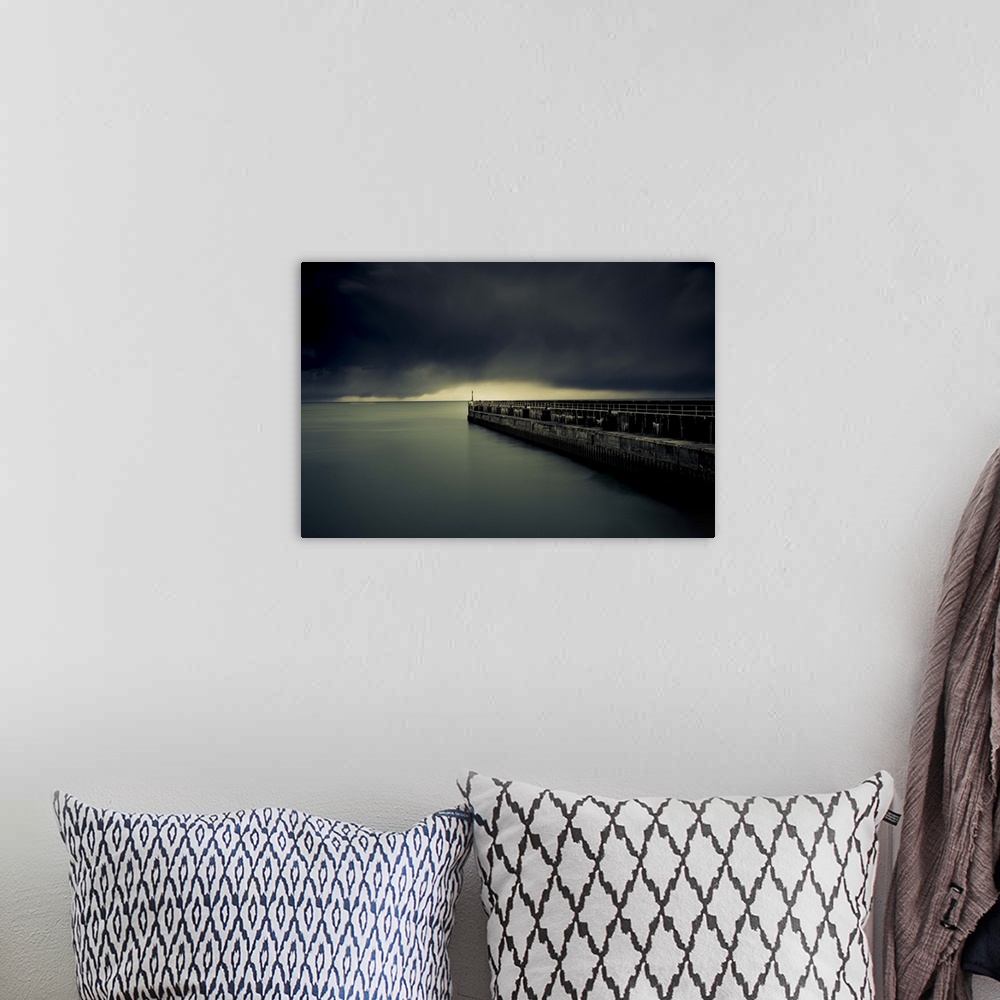 A bohemian room featuring A photograph of a pier jetting out over water under a sky filled with a blanket of dark clouds.