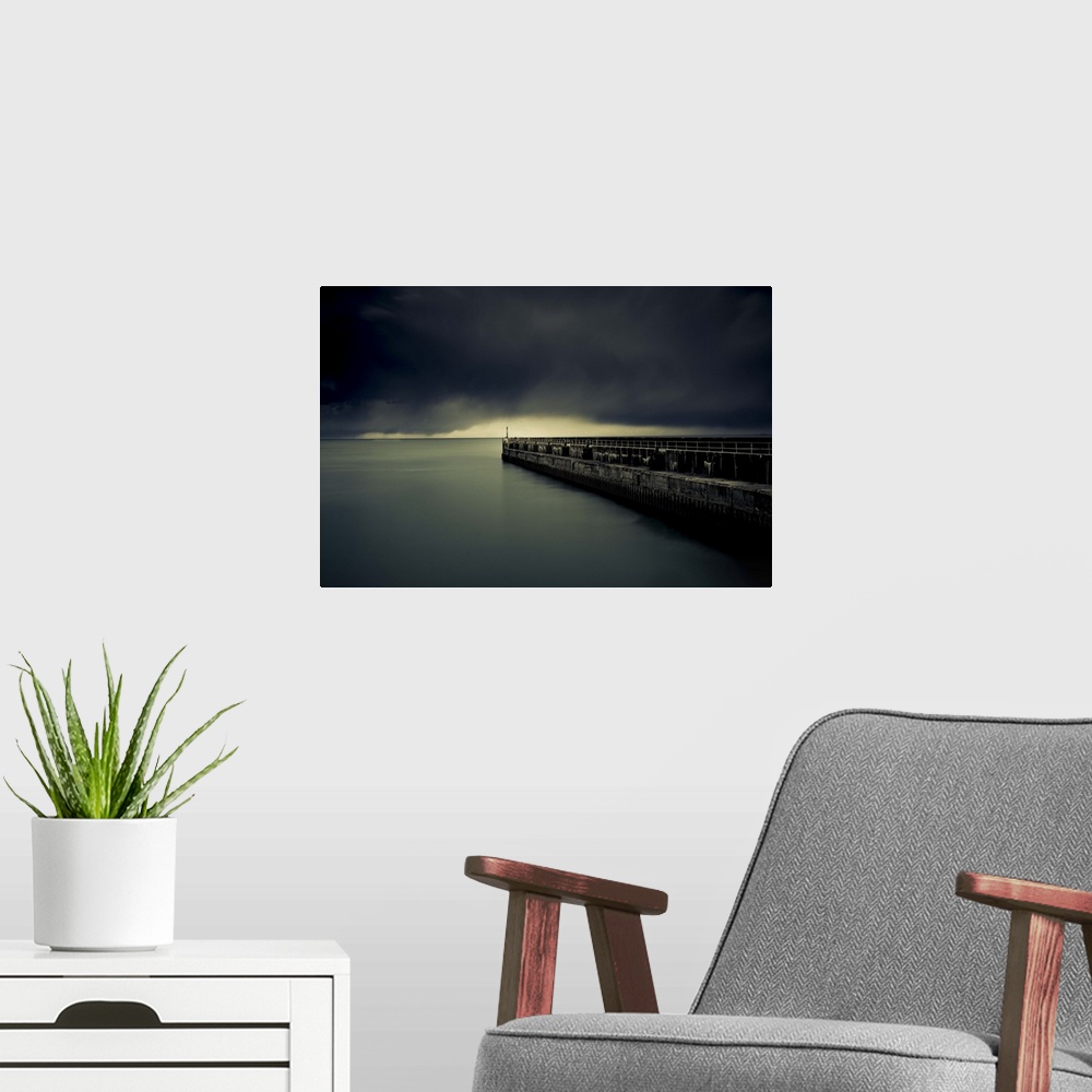 A modern room featuring A photograph of a pier jetting out over water under a sky filled with a blanket of dark clouds.