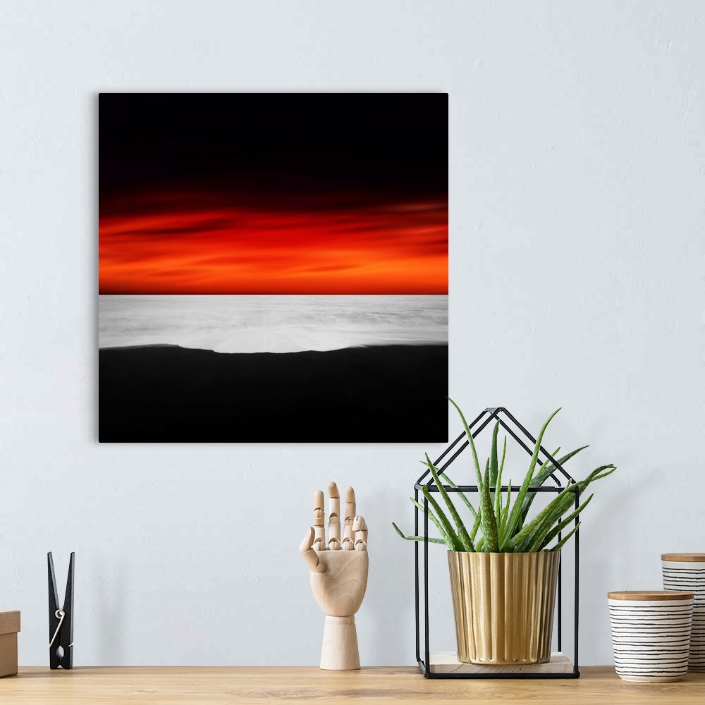 A bohemian room featuring A dramatic photograph of a blazing sky hanging over a white seascape seen from a black sand beach.