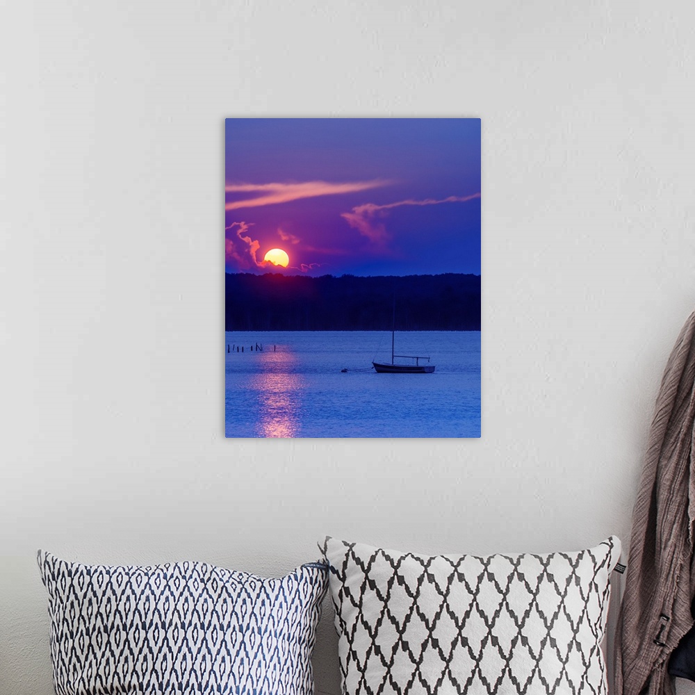 A bohemian room featuring The setting sun glowing vividly against the violet evening sky, over a lone boat on the water, at...