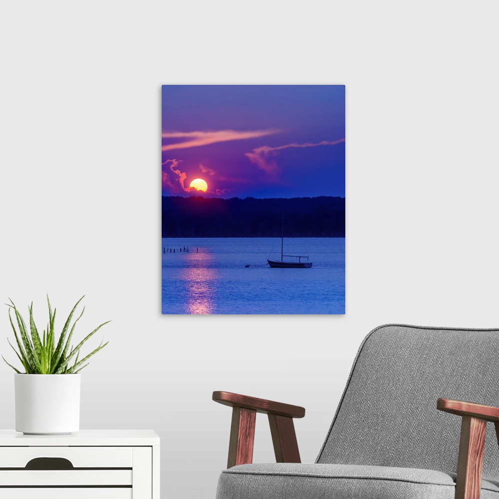 A modern room featuring The setting sun glowing vividly against the violet evening sky, over a lone boat on the water, at...