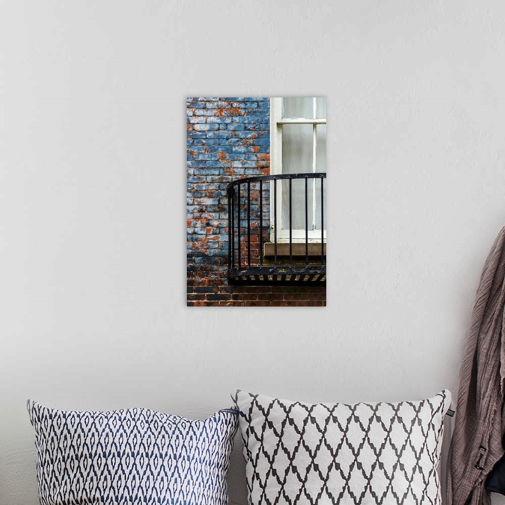 A bohemian room featuring A metal balcony under a window attached to a blue painted brick wall.