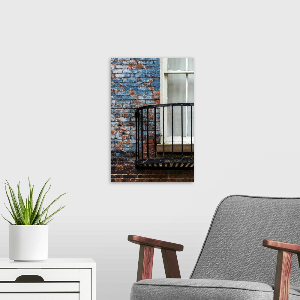 A modern room featuring A metal balcony under a window attached to a blue painted brick wall.