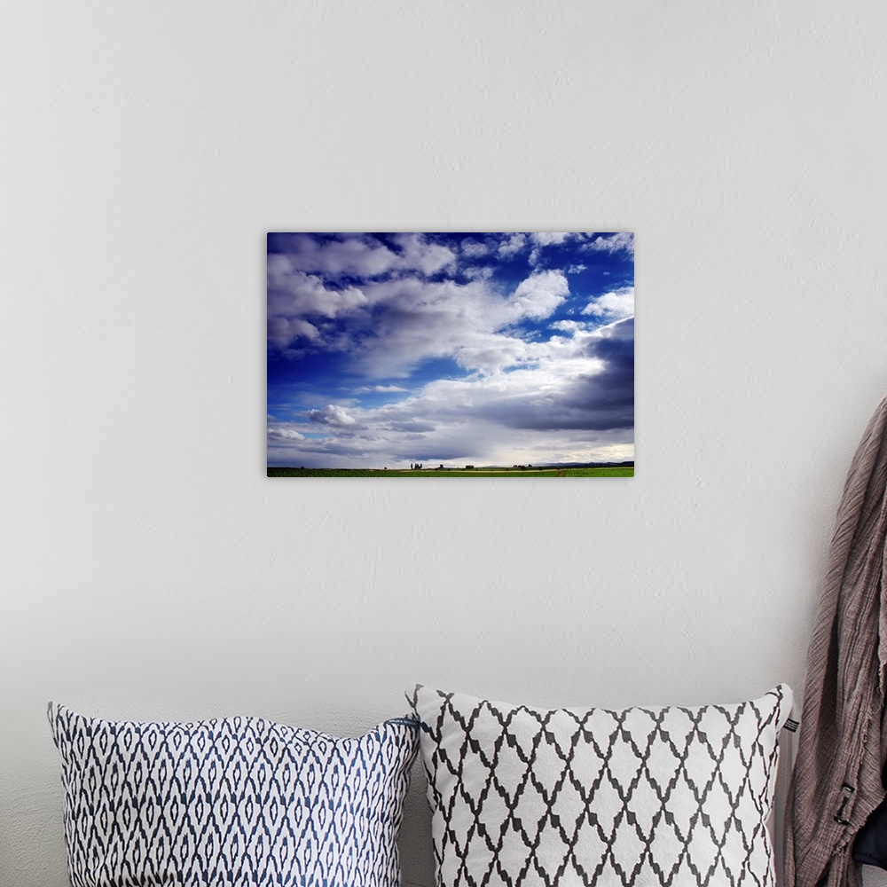 A bohemian room featuring Large horizontal photograph of many fluffy white clouds in a vibrant blue sky, over a green farm ...