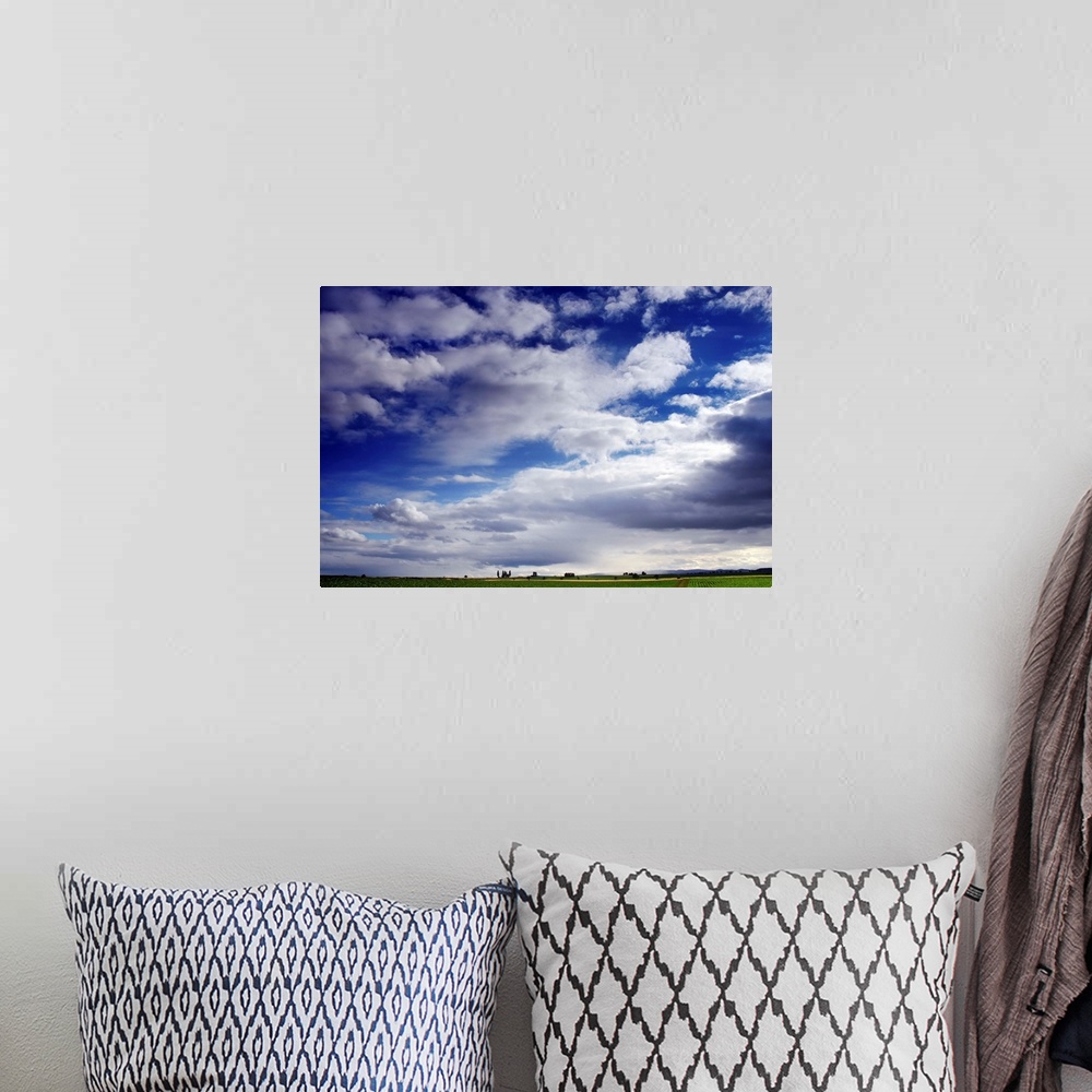 A bohemian room featuring Large horizontal photograph of many fluffy white clouds in a vibrant blue sky, over a green farm ...