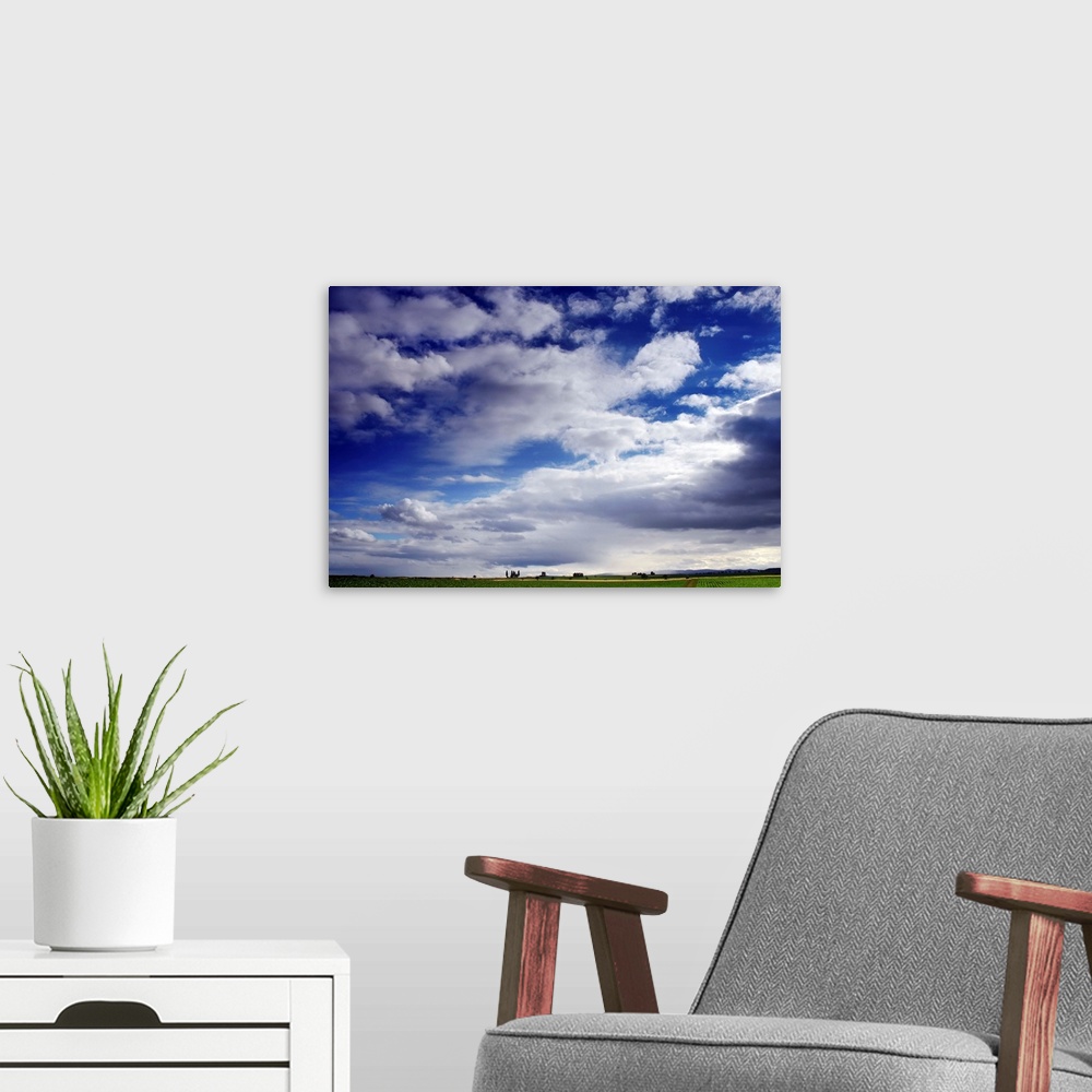 A modern room featuring Large horizontal photograph of many fluffy white clouds in a vibrant blue sky, over a green farm ...