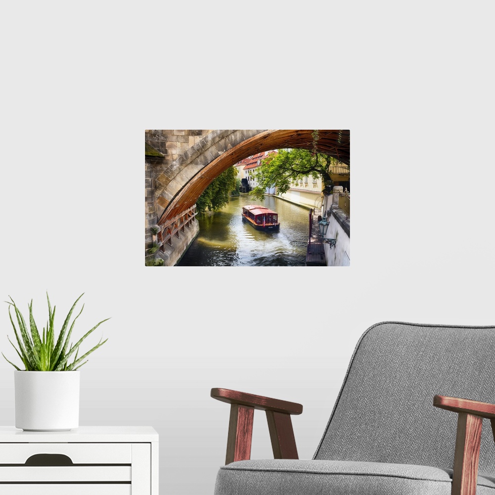 A modern room featuring A boat on the water passing under an arched bridge in Prague, Czech Republic.