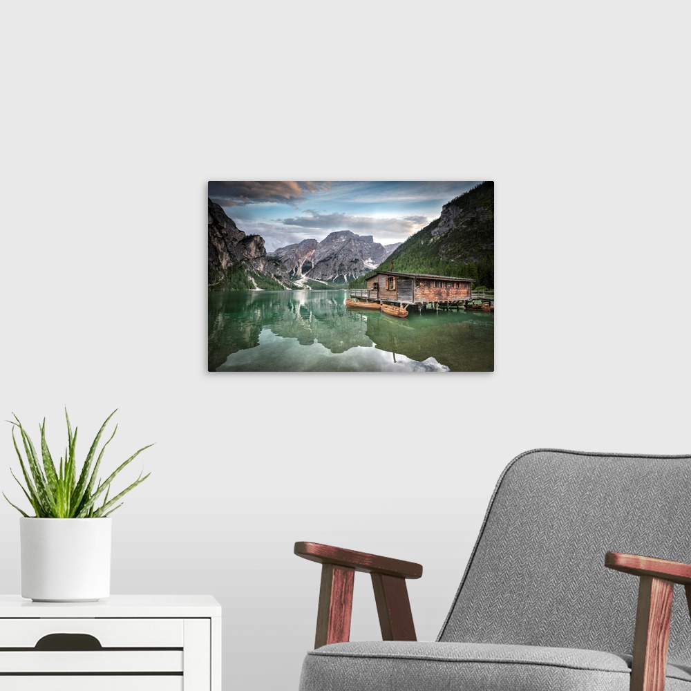 A modern room featuring Jade green lake reflecting mountainous valley and cabin.