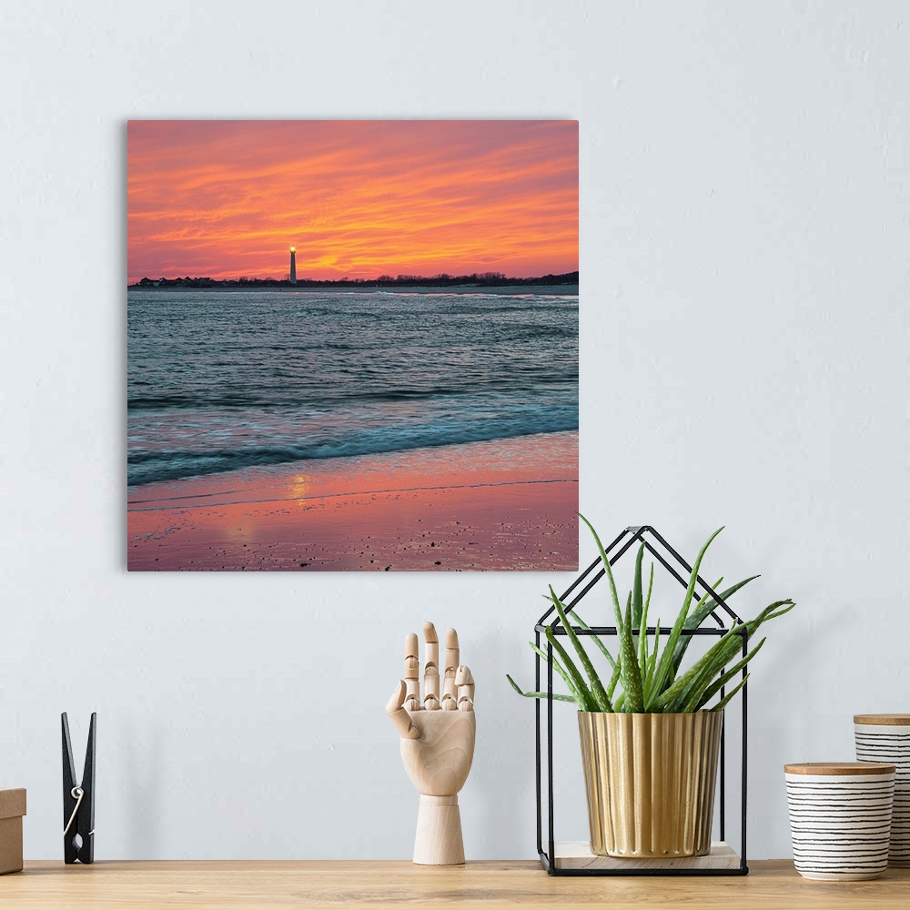 A bohemian room featuring Vivid orange sunset sky over the ocean at low tide, with Cape May lighthouse shining in the dista...