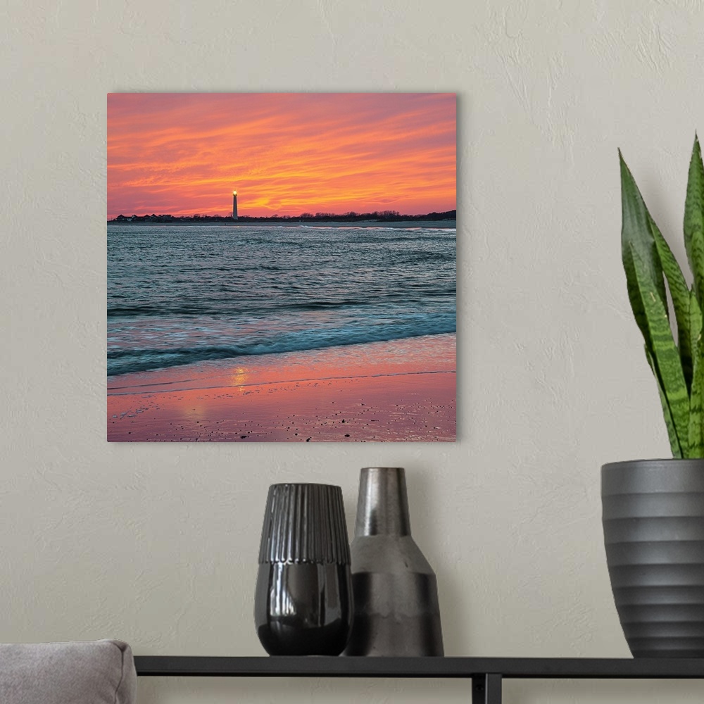 A modern room featuring Vivid orange sunset sky over the ocean at low tide, with Cape May lighthouse shining in the dista...