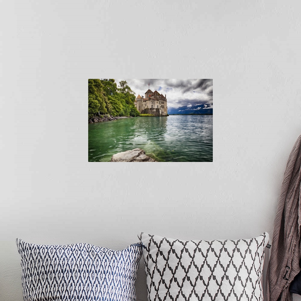 A bohemian room featuring The Chateau de Chillon on the edge of Lake Geneva, with the Alps in the distance on a cloudy day,...