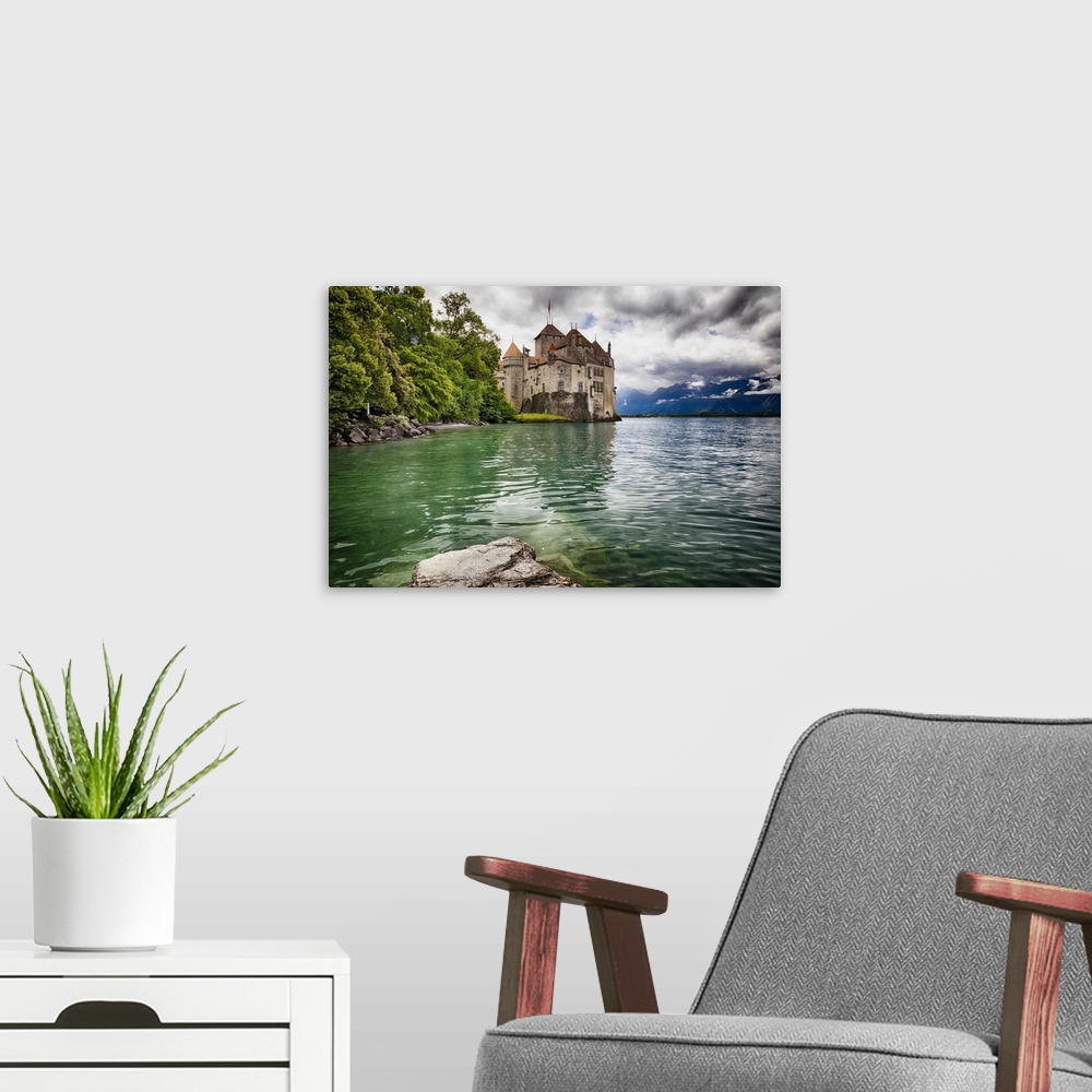 A modern room featuring The Chateau de Chillon on the edge of Lake Geneva, with the Alps in the distance on a cloudy day,...