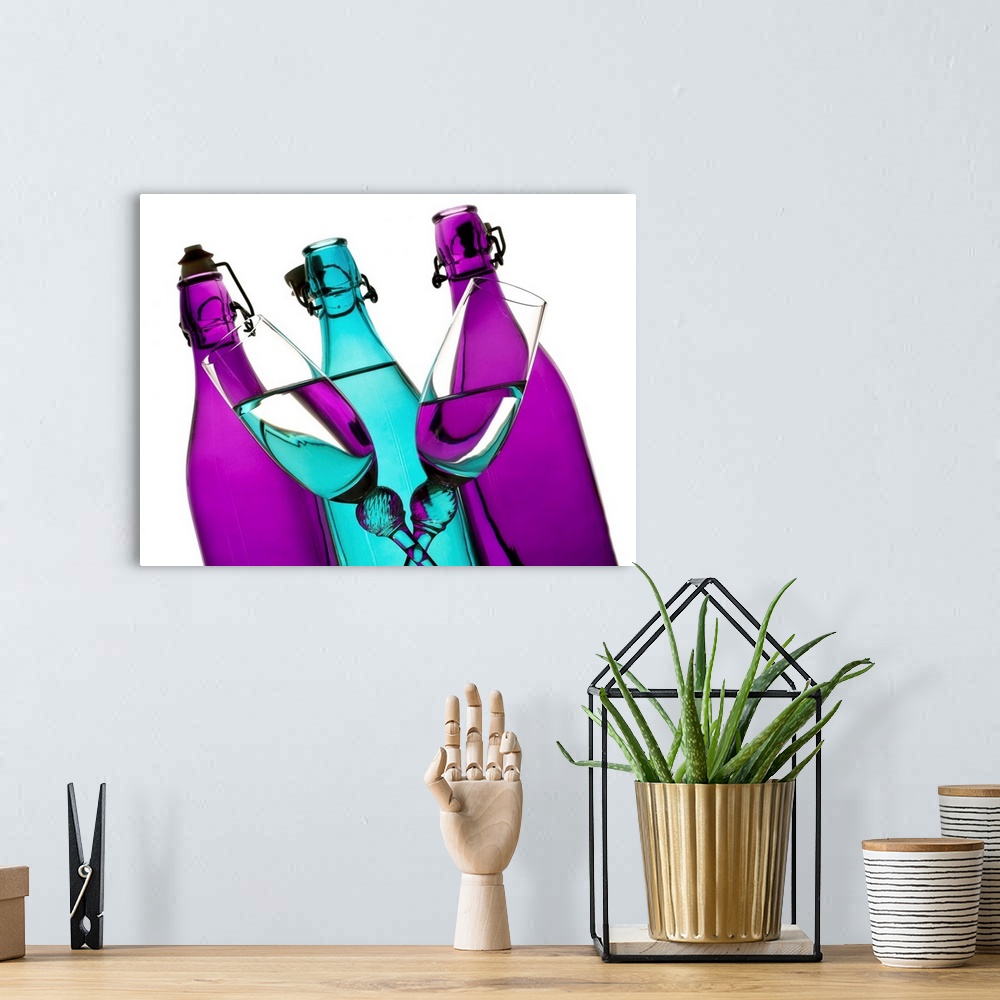 A bohemian room featuring turquoise and purple glass bottles with two champagne flutes crossing in front on a white backgro...