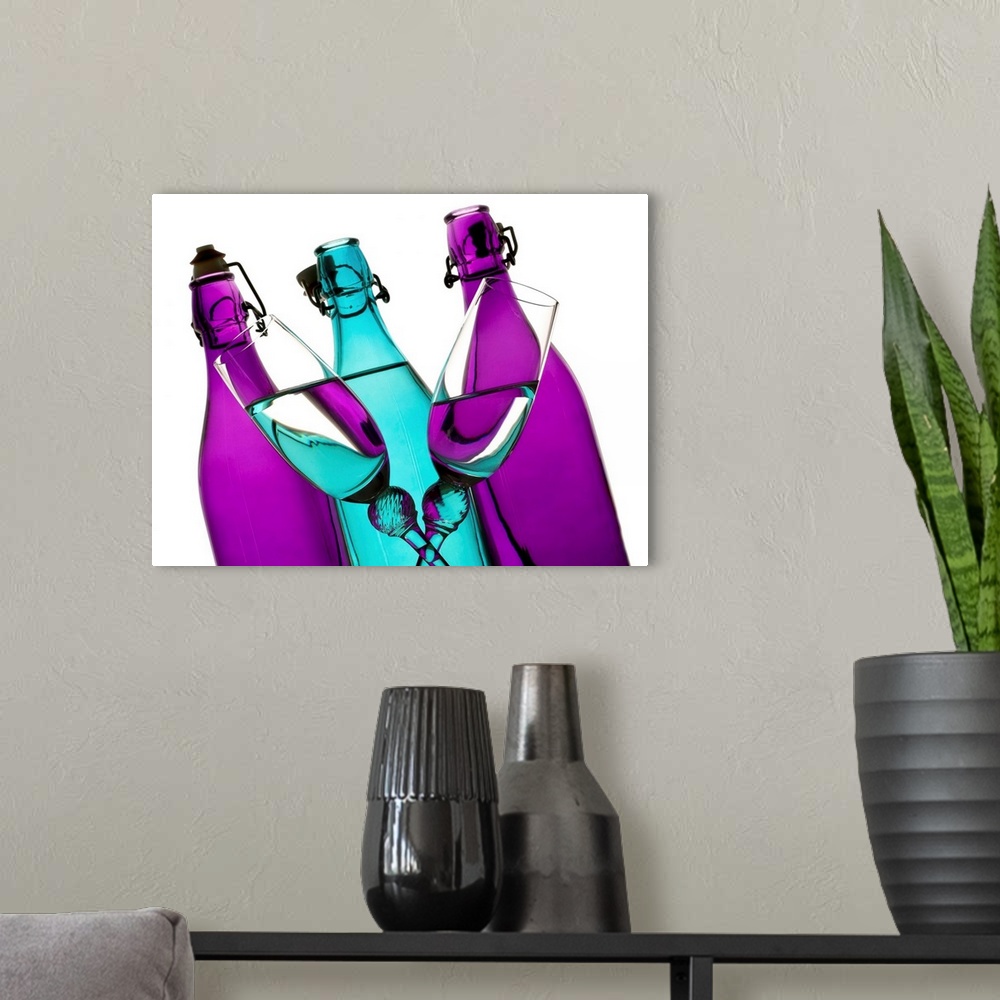 A modern room featuring turquoise and purple glass bottles with two champagne flutes crossing in front on a white backgro...