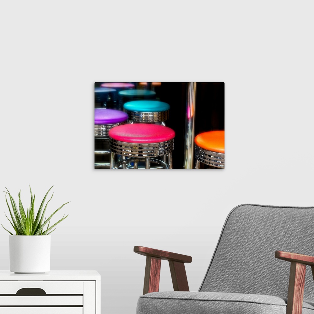 A modern room featuring Brightly colored bar stools in pink, purple, teal, and orange, with chrome rims.