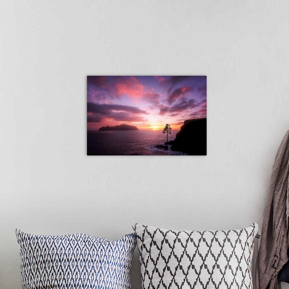A bohemian room featuring Rocky cliffs on the ocean under a cloudy sky lit up with sunset light.
