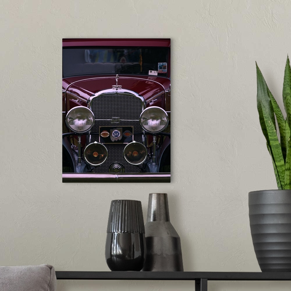 A modern room featuring The front grille and round headlights of a maroon colored vintage car.