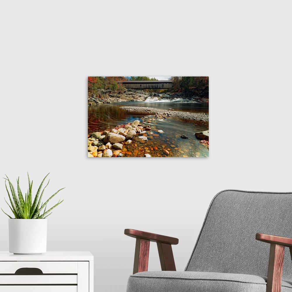 A modern room featuring A rocky riverbed in New Hampshire with the Swiftwater Covered Bridge in the distance.