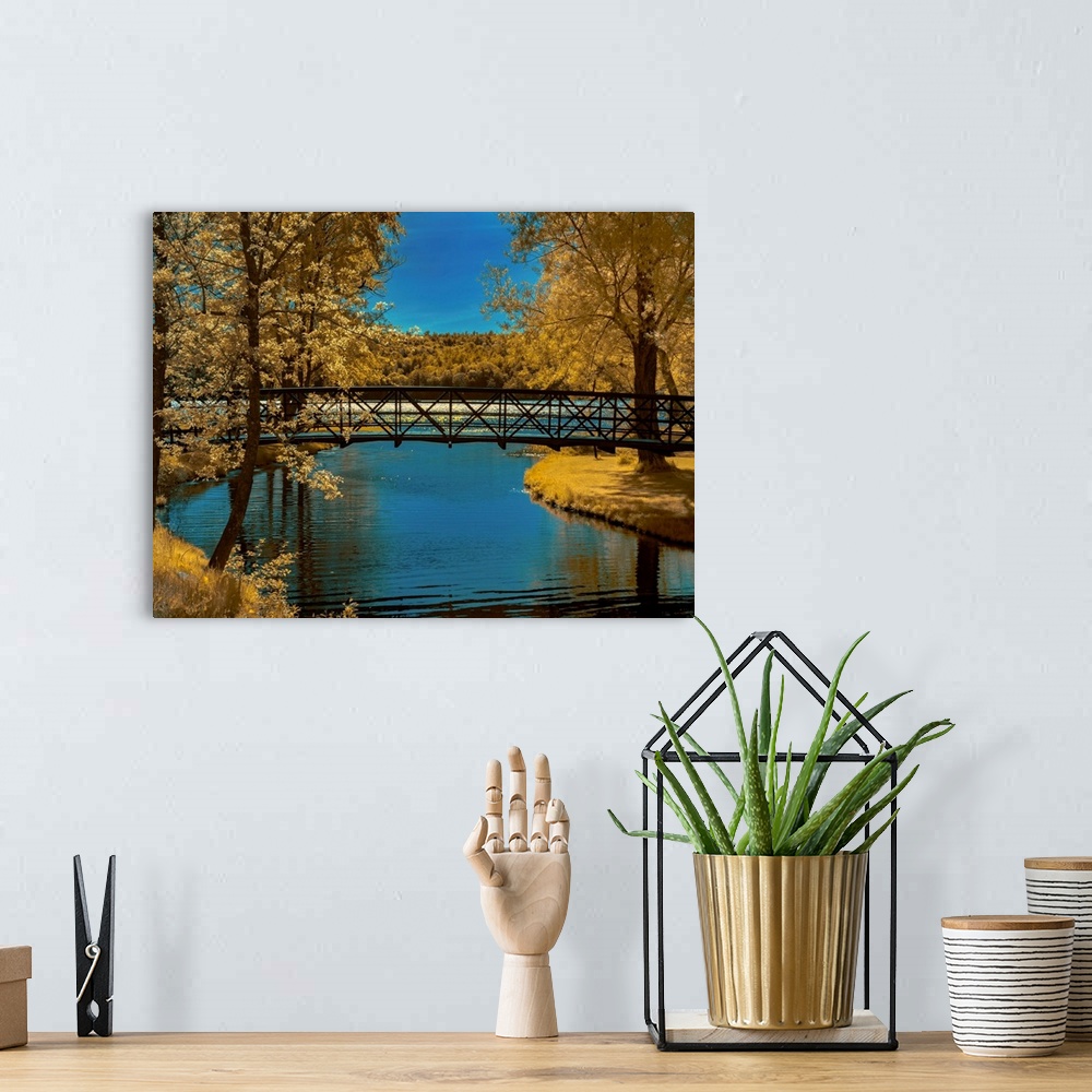A bohemian room featuring Long bridge over a river lined with Autumn colored trees and grass.