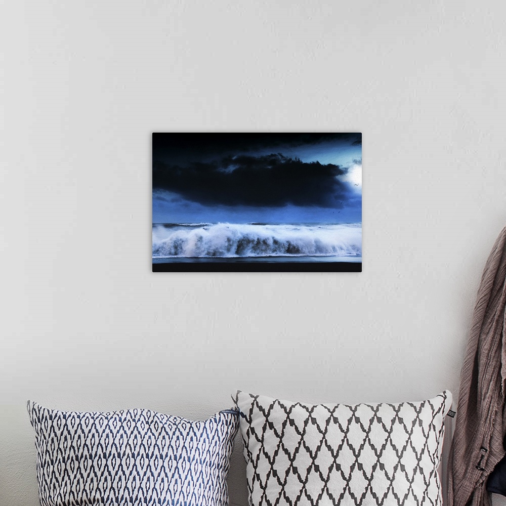 A bohemian room featuring A photograph of a seascape under a dark cloudy sky.