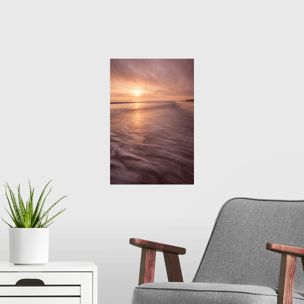 A modern room featuring A calm saescape at dawn with a glowing peach sky reflecting in the sea with swooshing waves.