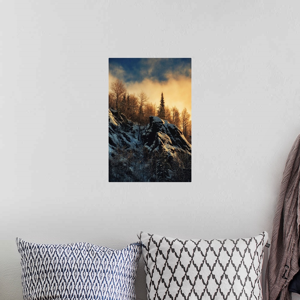 A bohemian room featuring Clouds lit up with fading sunlight over a forest near snowy rocks on a mountainside.