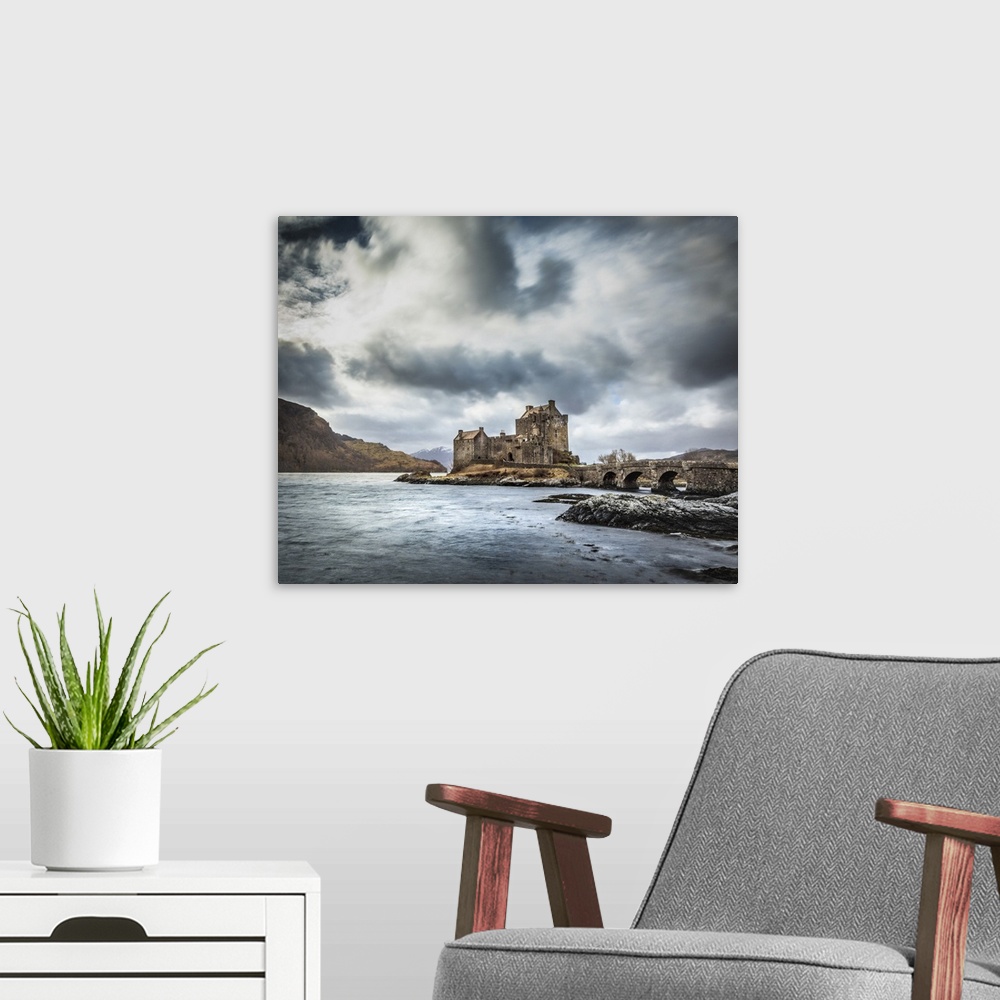 A modern room featuring Scottish Castle Eilean Donan with a moody grey sky and light blue waves with a bridge in the fore...