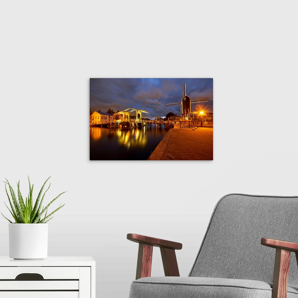 A modern room featuring View of a canal with a small bridge and windmill at night, Leiden, South Holland, Netherlands.